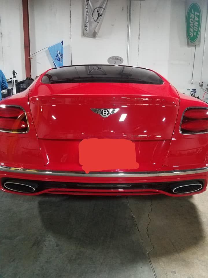 Rear view of a red Bentley sports car parked indoors, showing the trunk and taillights.