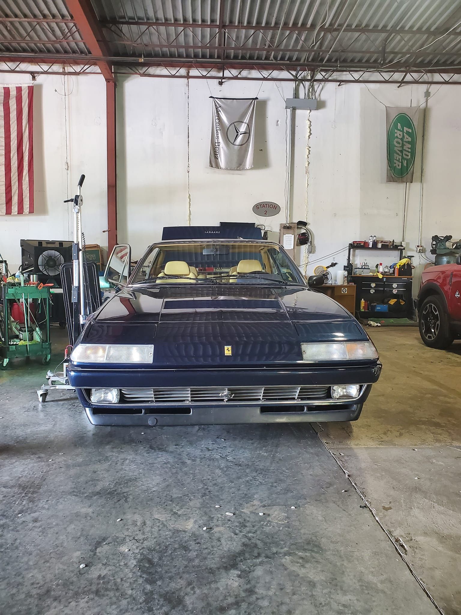 Classic dark blue convertible car parked inside a garage with tools and other vehicles nearby