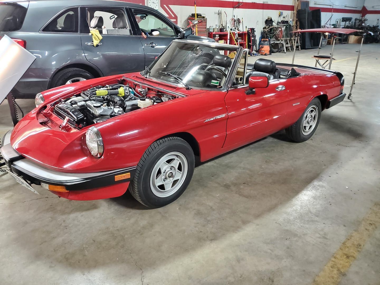 Red convertible sports car with hood open in a garage, showing the engine