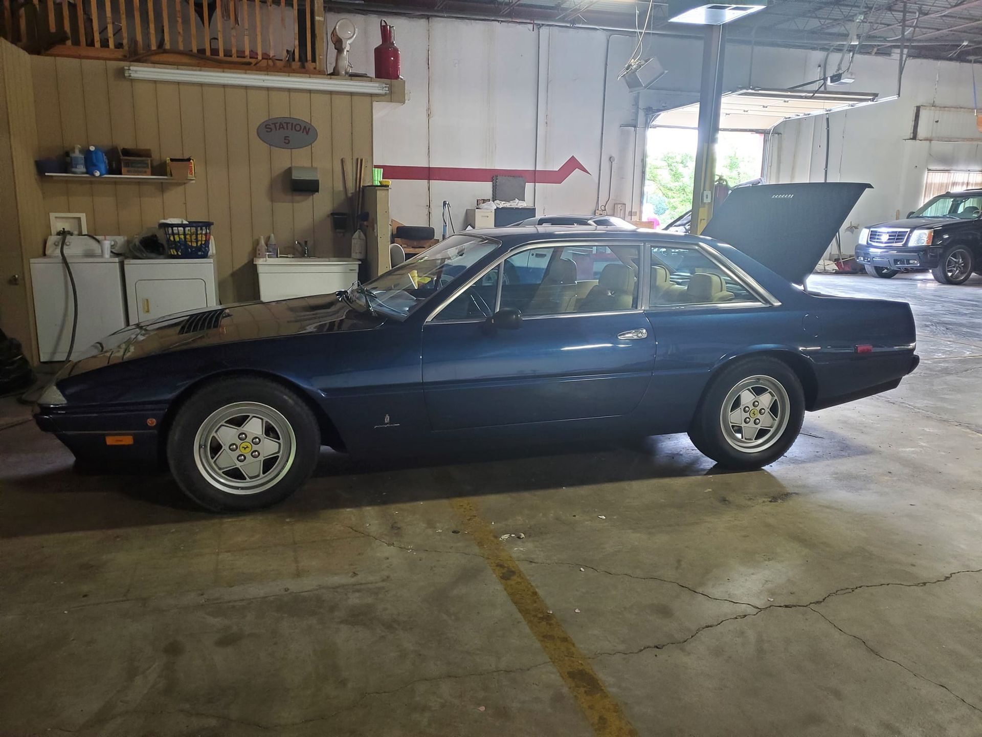 Dark blue classic car parked inside a garage next to another vehicle.