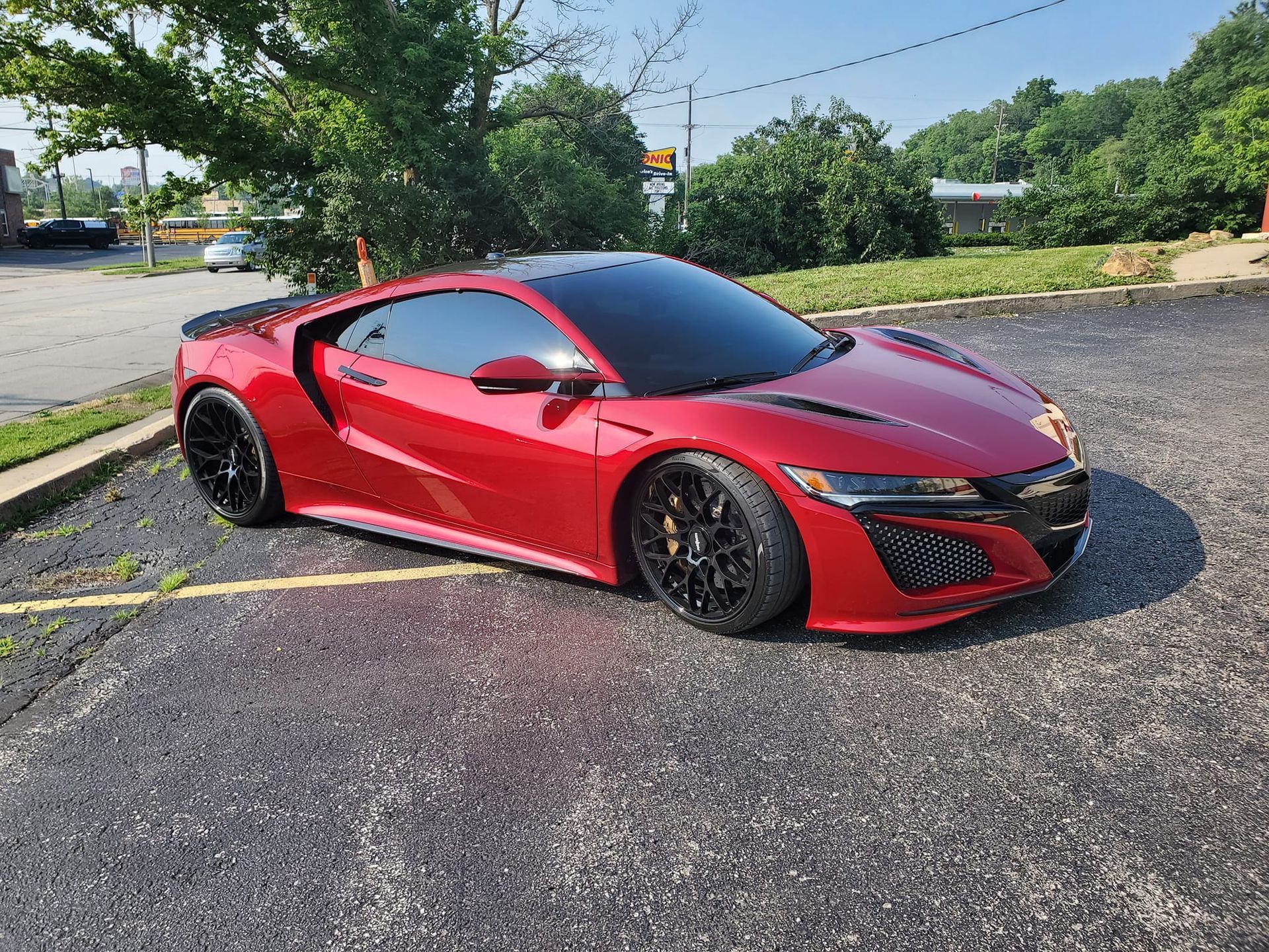 Red sports car parked on a gravel lot beside trees and a road.
