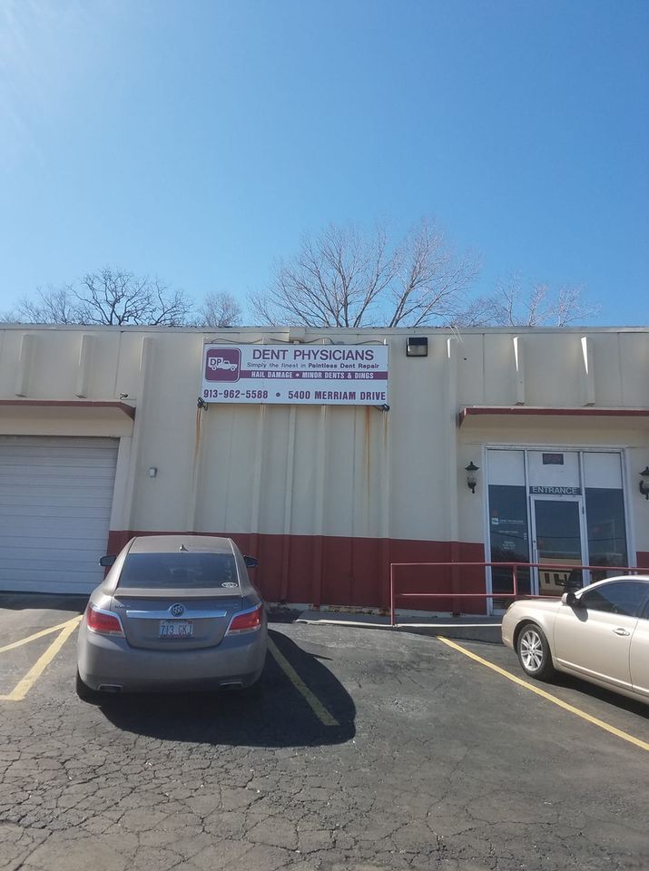 Commercial storefront with parking lot, blue sky, and two parked cars outside.