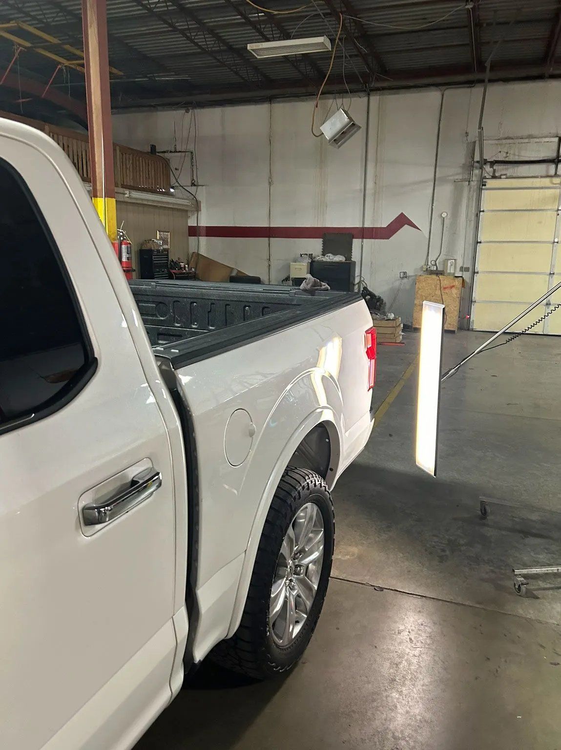 White pickup truck parked indoors near a bollard in a warehouse or garage.