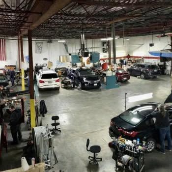 Busy auto repair shop with several cars, mechanics, and tools in a large garage.