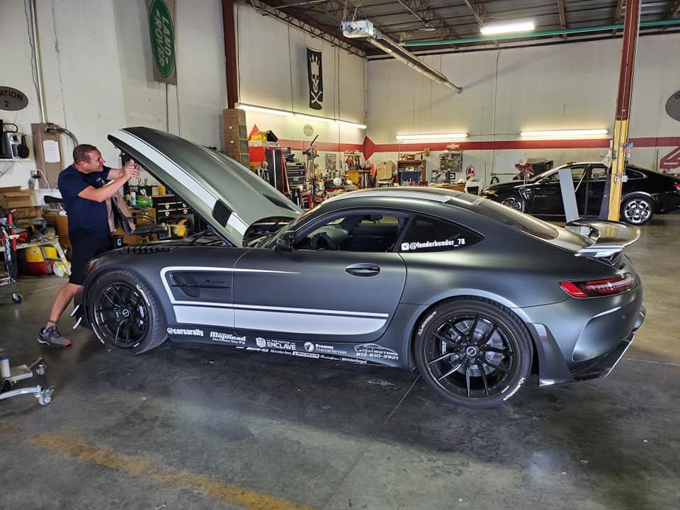 Gray sports car with hood open in a garage, mechanic standing beside it.