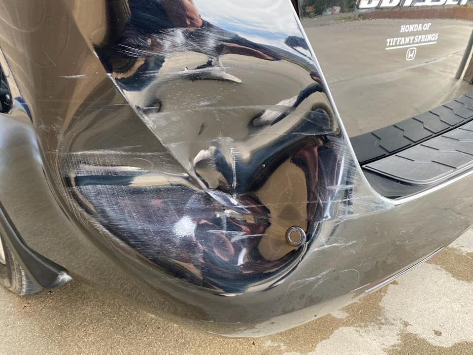 Crushed rear bumper and taillight area of a gray car, with a cracked panel near the tire.