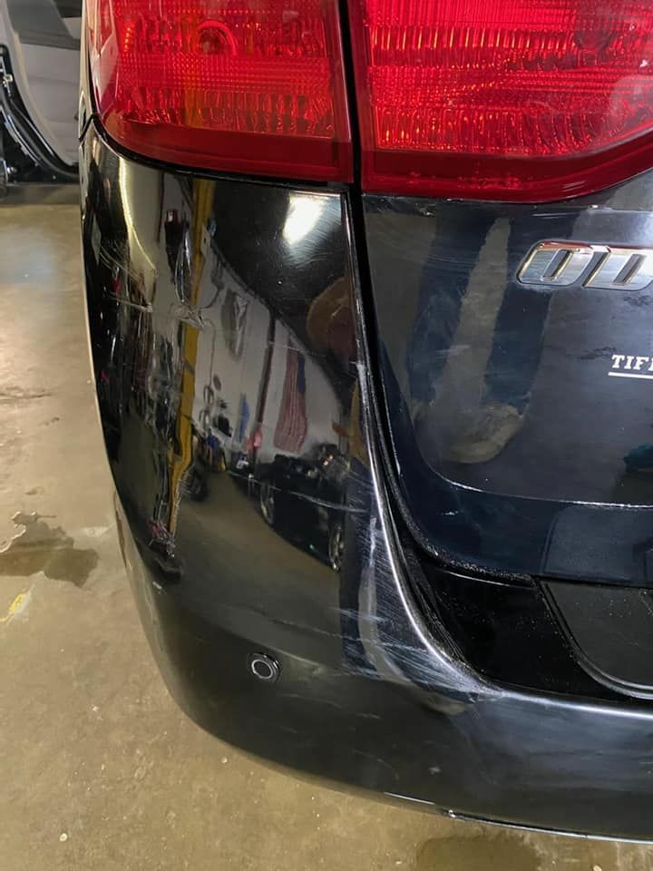 Close-up of a black car’s rear bumper with a red taillight and visible scratch or dent mark.