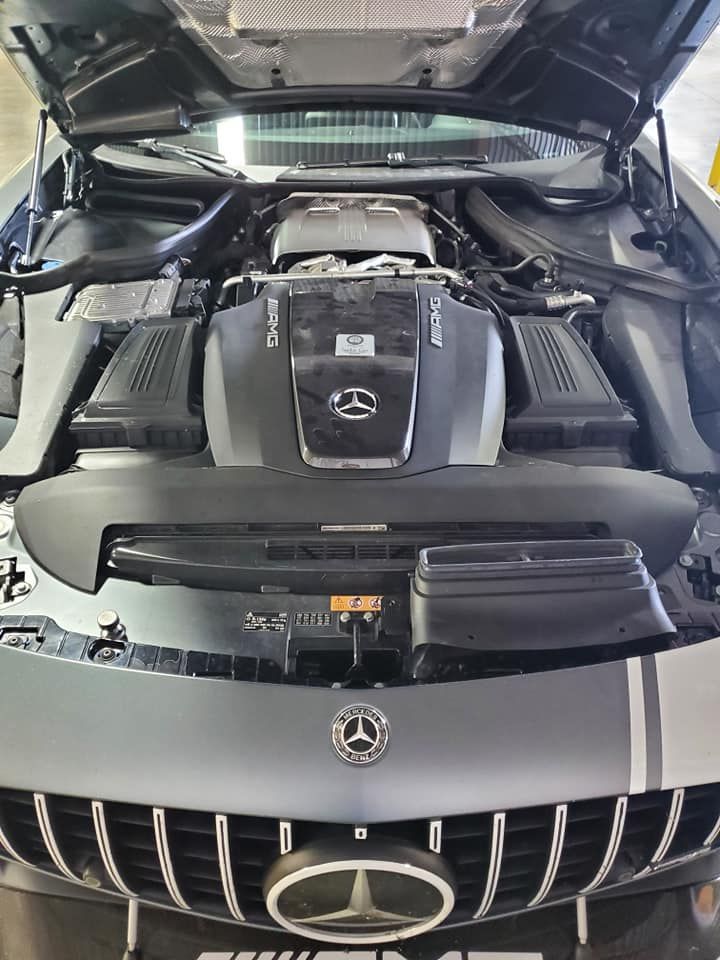 Open car hood showing a Mercedes-Benz engine bay with black and silver components.