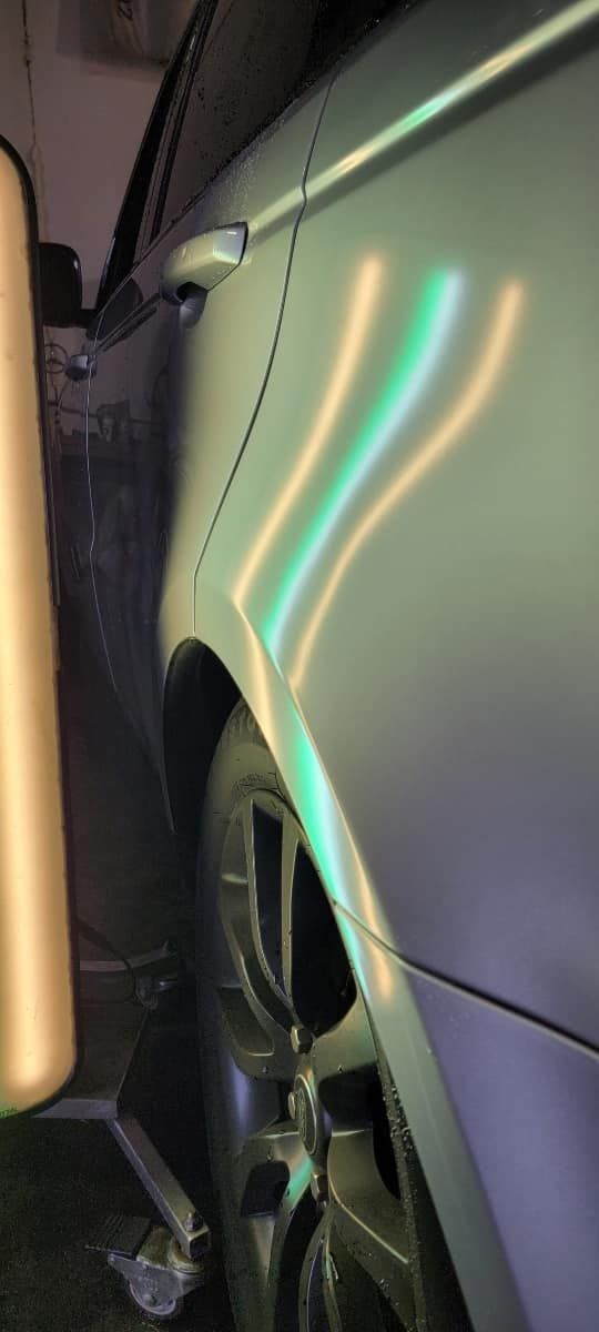 Close-up of a car’s side door and wheel with neon light reflections in a dark garage