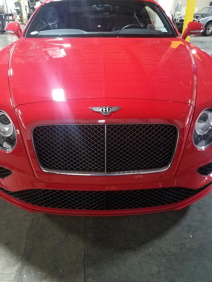 Front view of a red Bentley car with a large black mesh grille indoors.