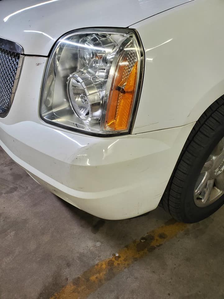 Close-up of a white vehicle’s front corner with headlight and amber turn signal in a parking garage.
