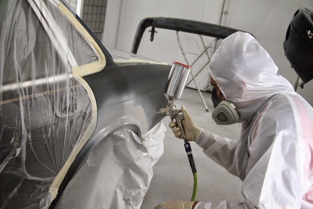 Worker in white protective suit spray-painting a car body in a paint booth.