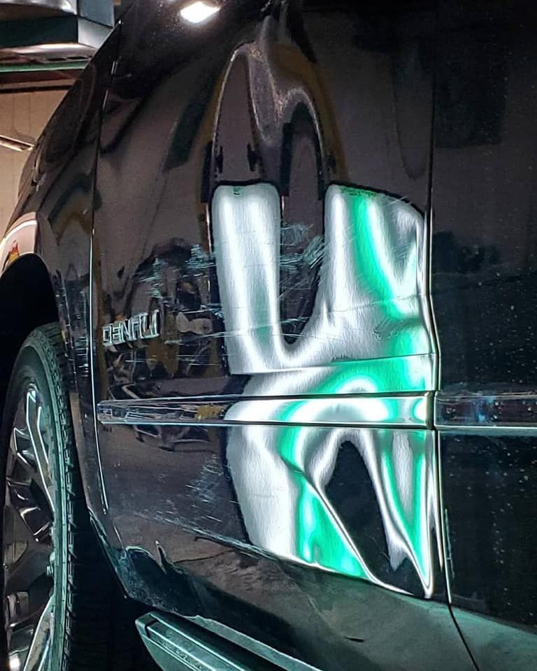 Close-up of a black car door with a bright turquoise and white graffiti-style reflection/paint design