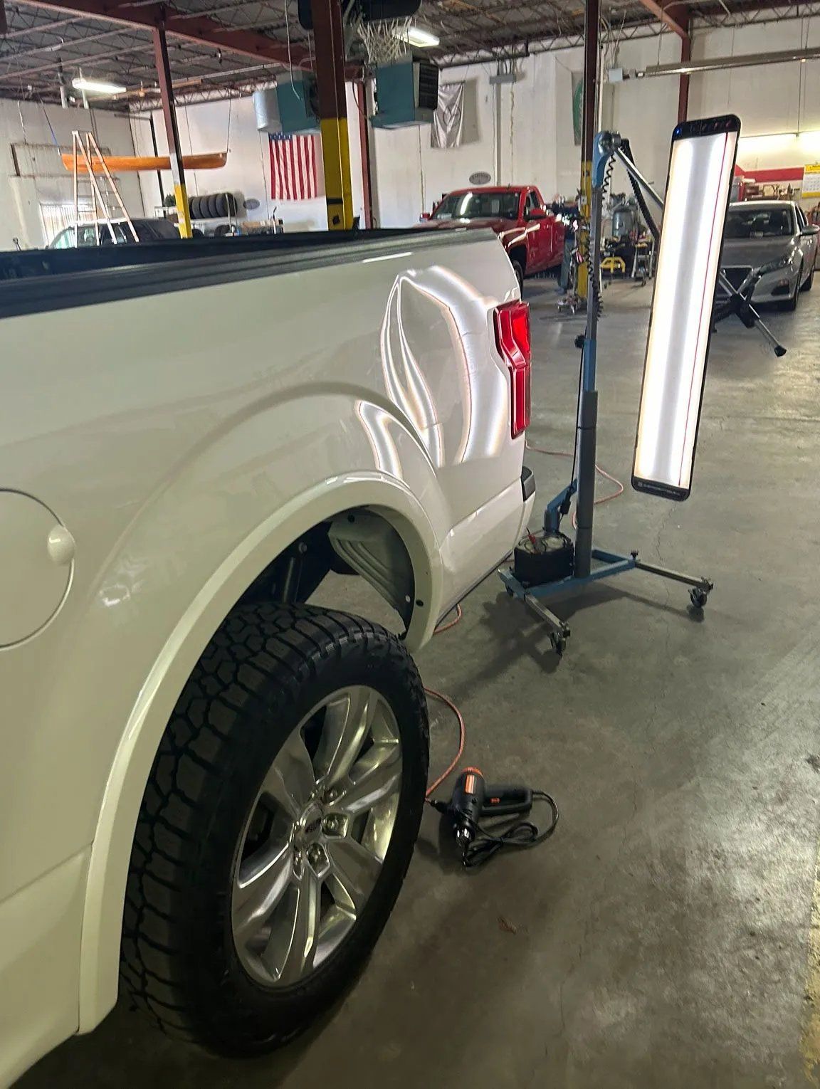 White pickup truck in an auto shop with a wheel alignment tool beside the rear wheel