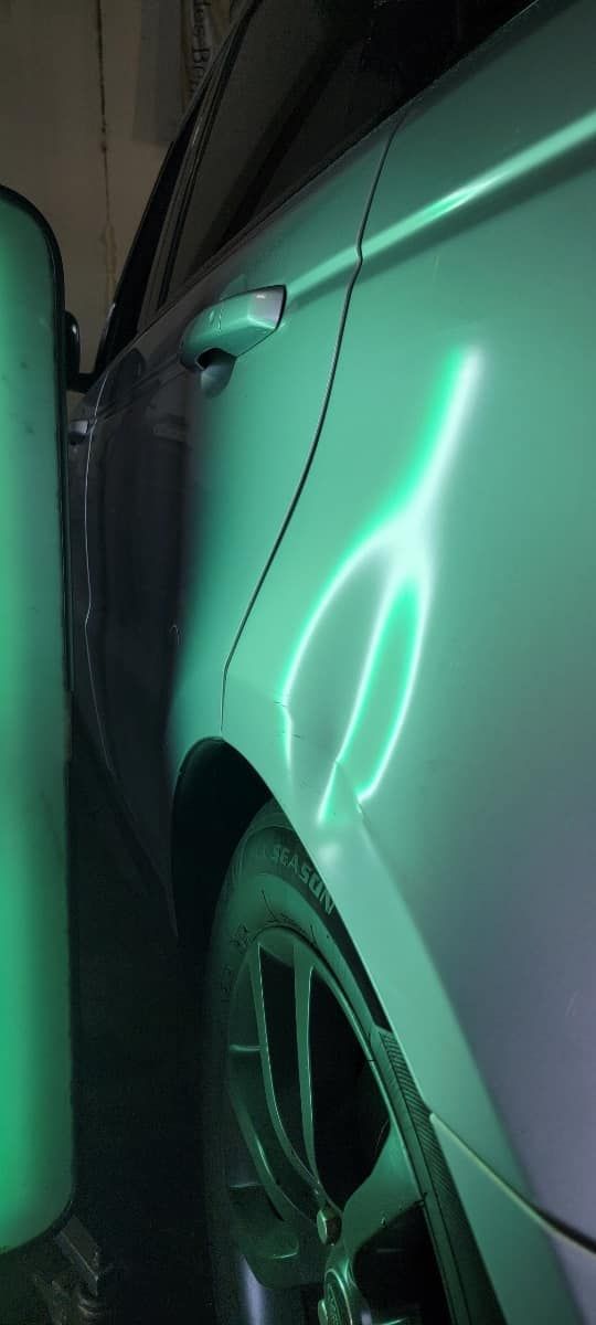 Close-up of a silver car door and wheel with green reflections in a narrow garage