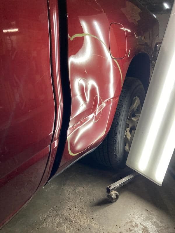 Red car with a dented door beside a bright work light in a garage