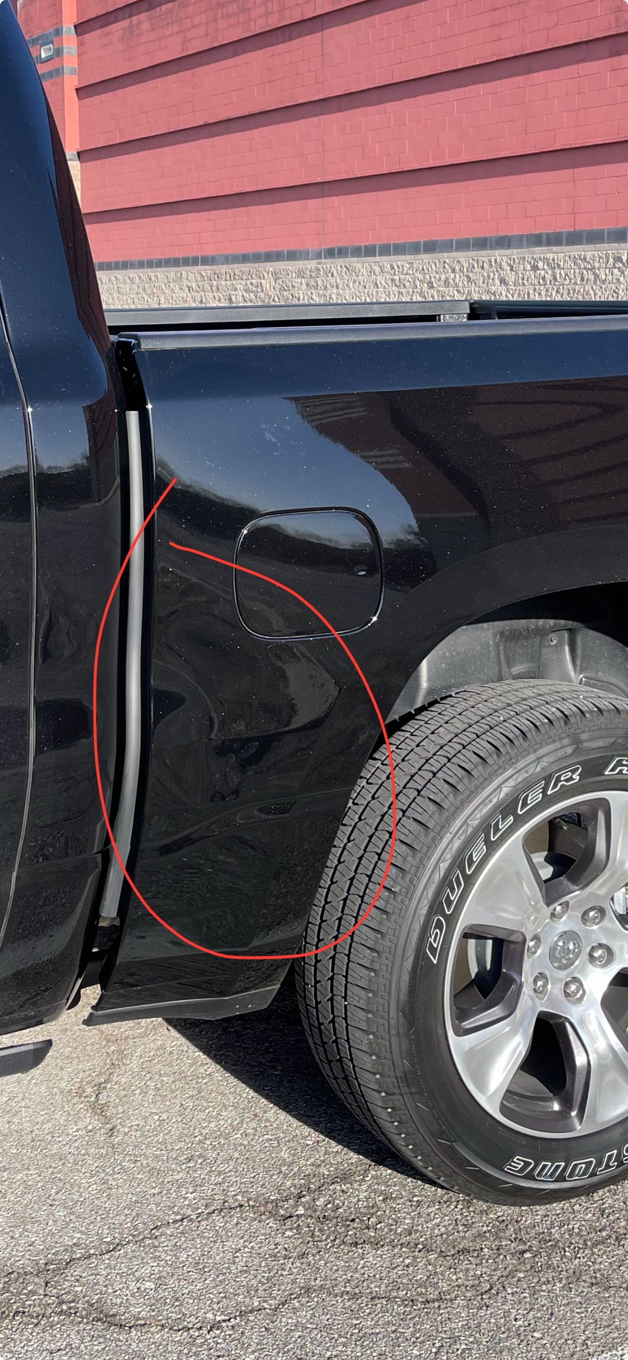 Side of a black truck parked beside red siding, with a red circle highlighting the rear wheel area.