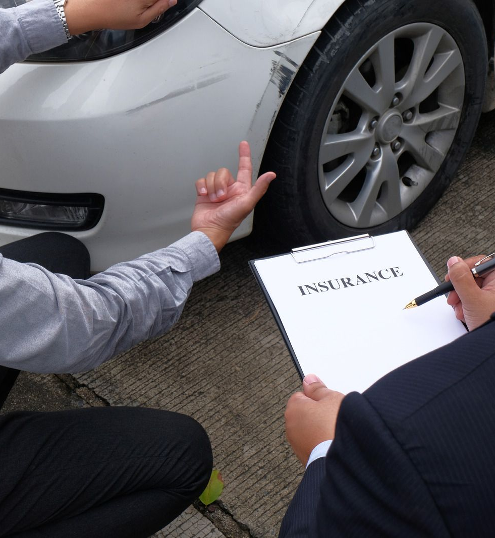 Car accident damage being inspected by an insurance adjuster beside a silver car