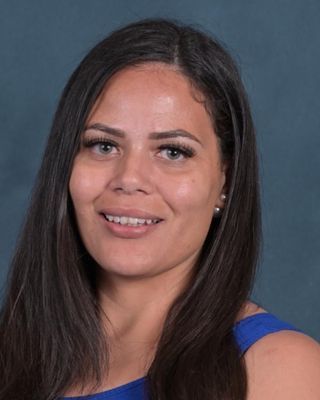 Woman with long dark hair, wearing a blue top, smiling at the camera.
