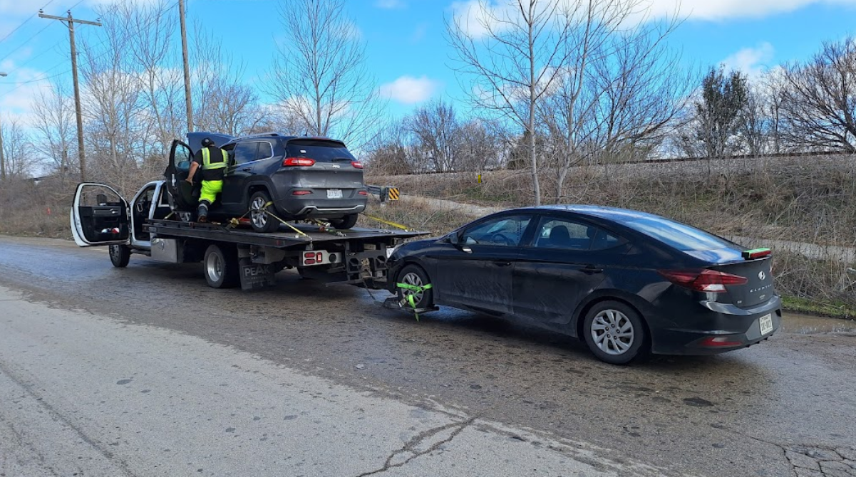 A black car is being towed by a tow truck.