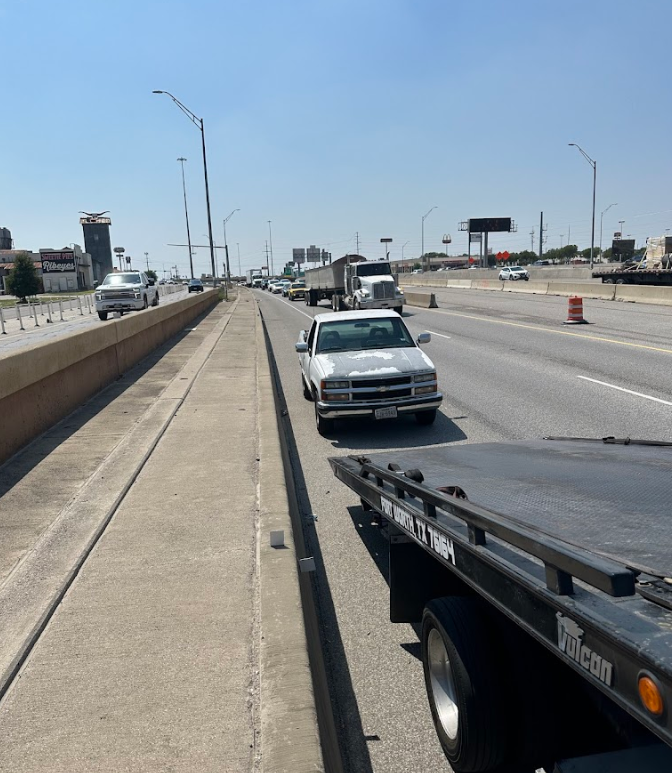 A white car is driving down a highway next to a tow truck