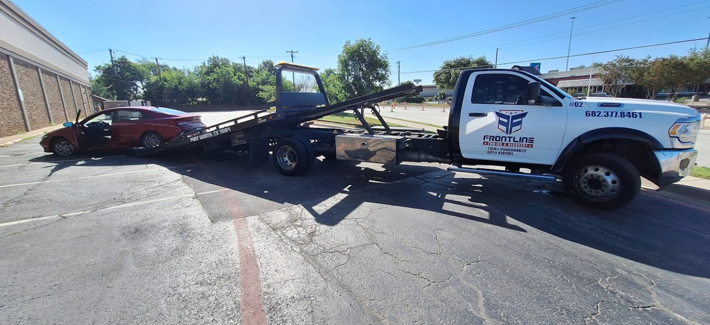 A tow truck is towing a red car on the side of the road.