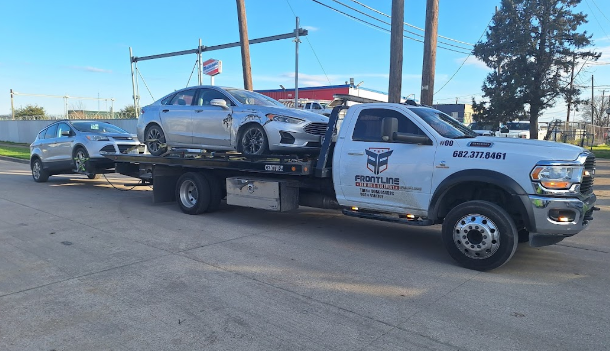 A tow truck is carrying two cars on the back of it.