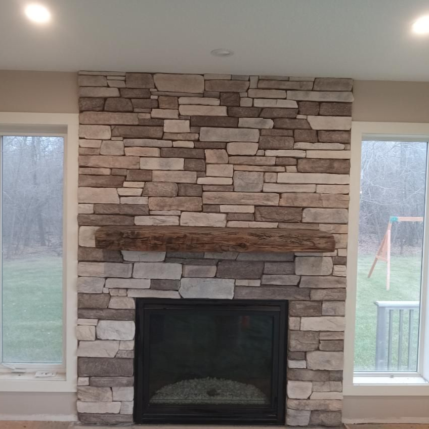 Stone fireplace with dark firebox between two tall windows in a living room