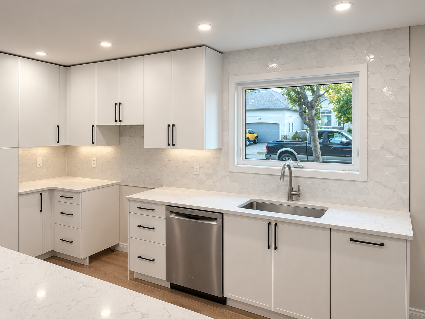 Bright modern white kitchen with cabinets, marble counters, sink, dishwasher, and window over the sink