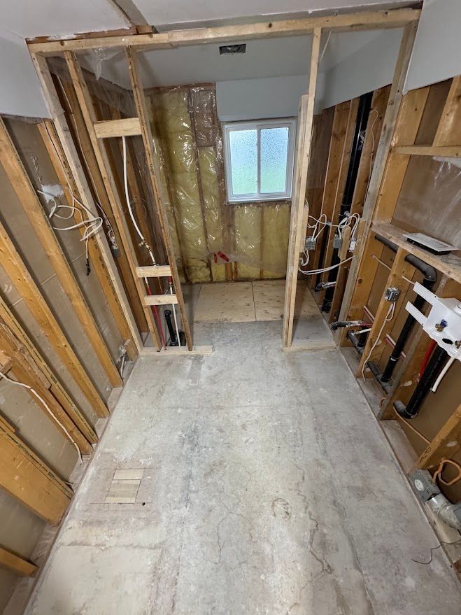 Interior under renovation with exposed wall studs, insulation, and a small window at the far end.
