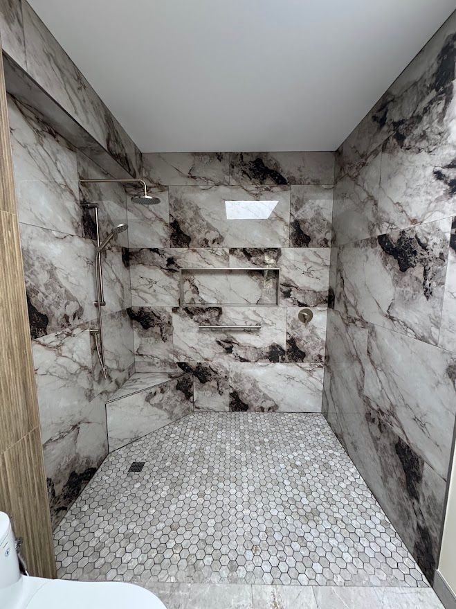 Marble-tiled shower with built-in shelves and pebble stone floor, lit by a small window.