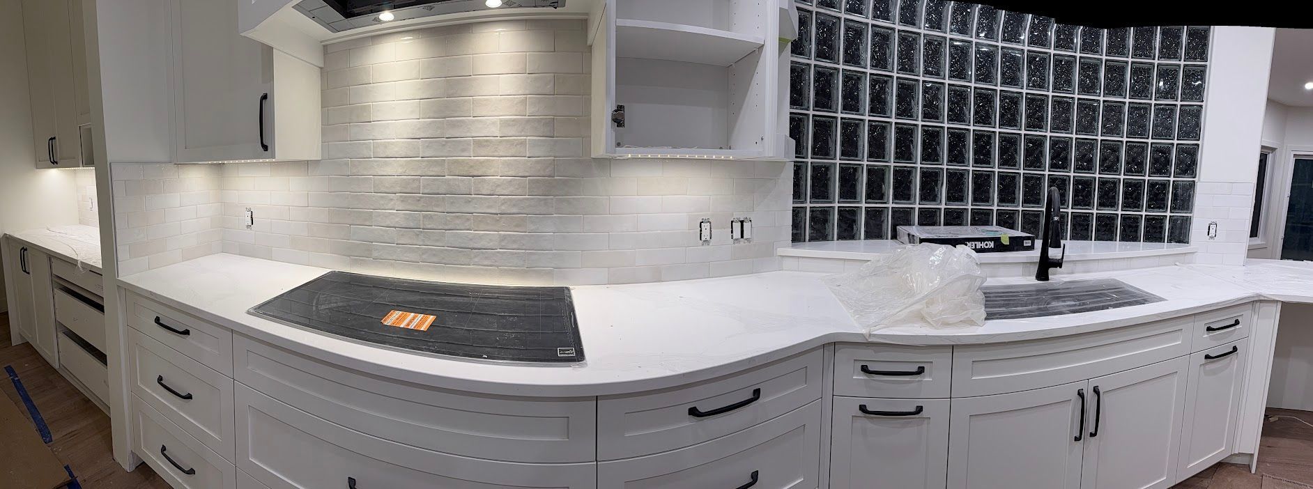 White kitchen with large island, dark countertops, white cabinets, and a grid backsplash structure