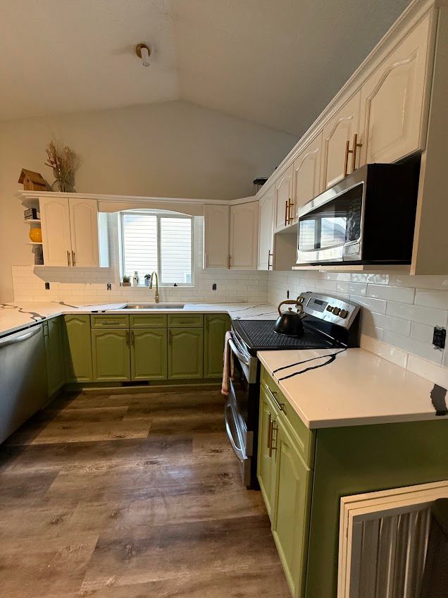 Bright kitchen with green lower cabinets, white uppers, stainless appliances, and a wood floor.