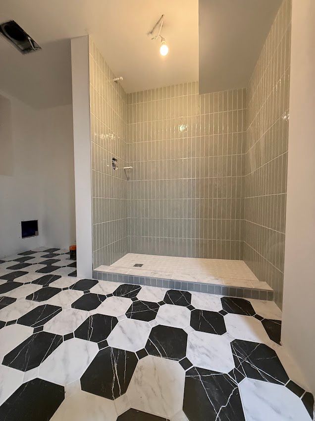 Empty tiled shower area with beige walls and black-and-white patterned floor tiles