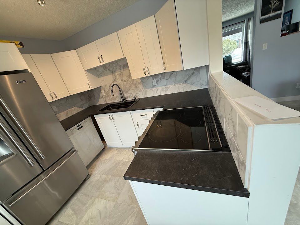 Compact kitchen with white cabinets, stainless fridge, and dark countertops, viewed from the entryway