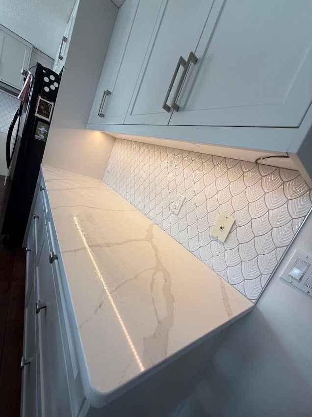 Modern white kitchen countertop with gray cabinets and patterned backsplash under under-cabinet lighting