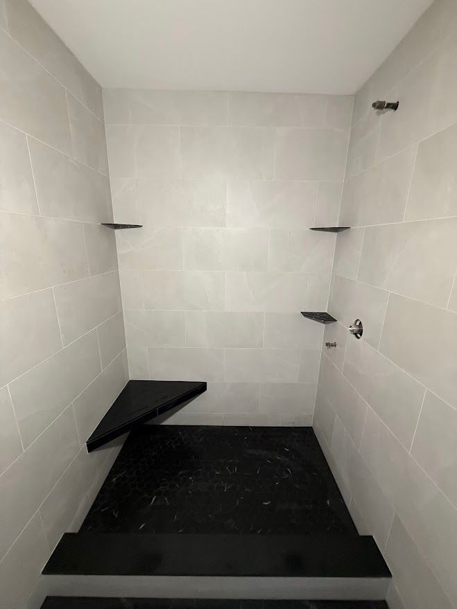 Empty tiled shower stall with black floor and small corner shelf
