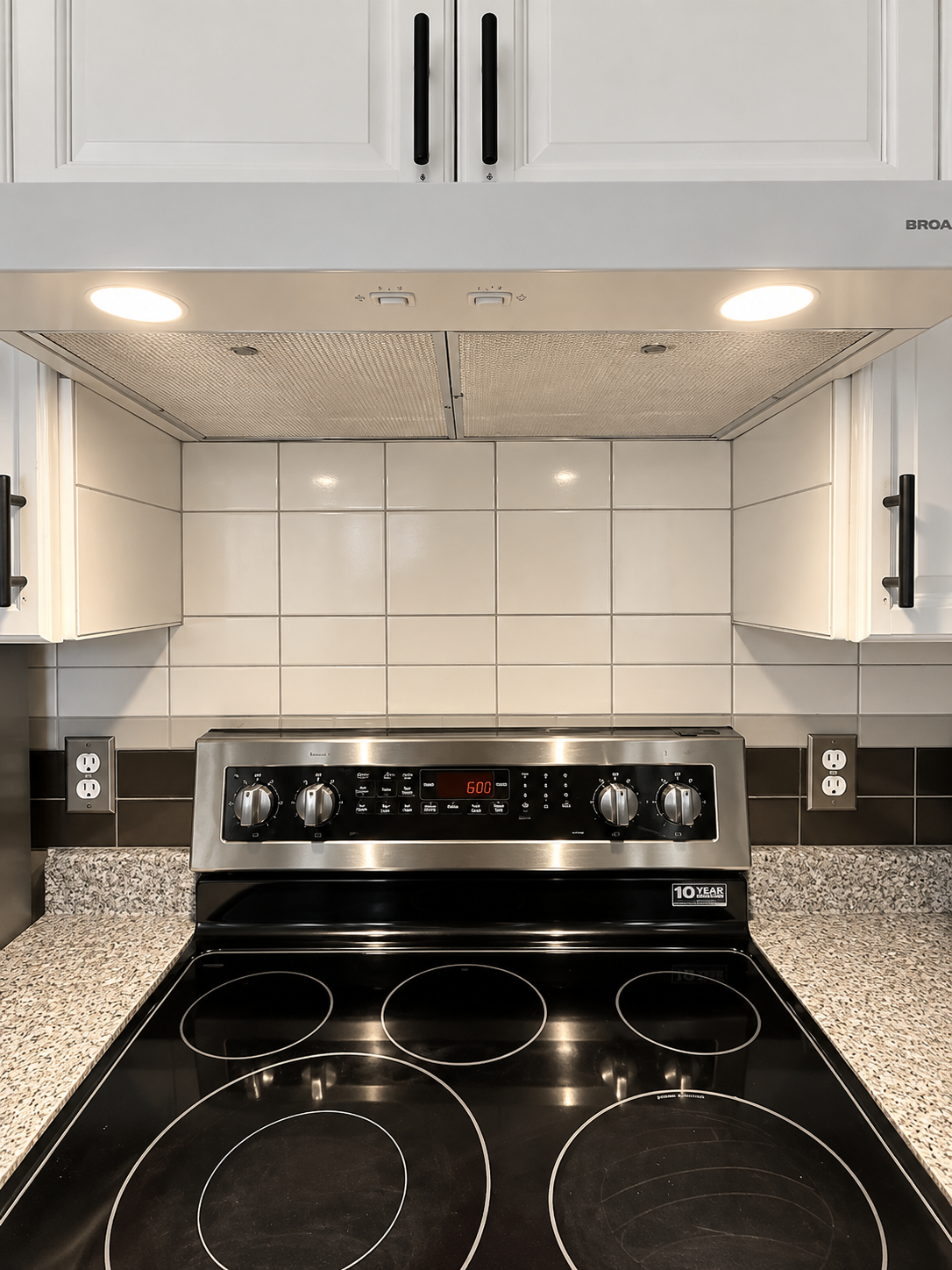 Modern kitchen stove with black cooktop, stainless steel range, white tile backsplash, and under-cabinet lighting