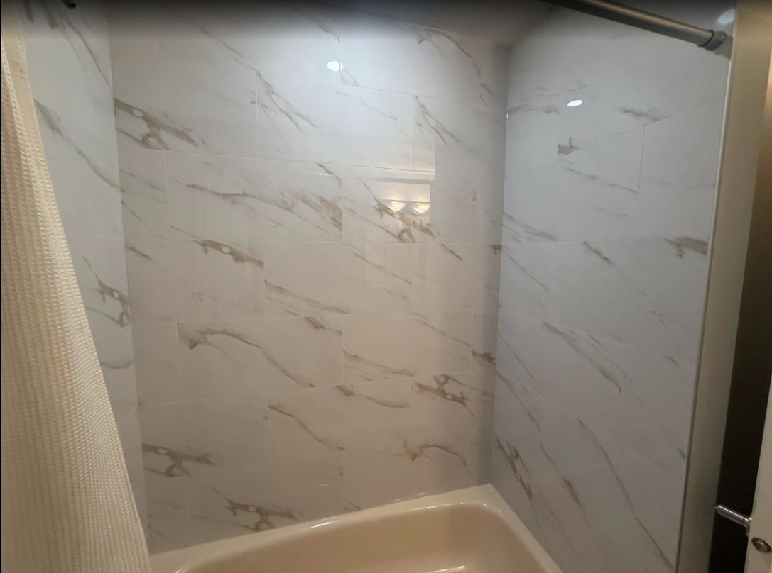 Empty shower stall with beige marble-pattern tile and a partial shower curtain.