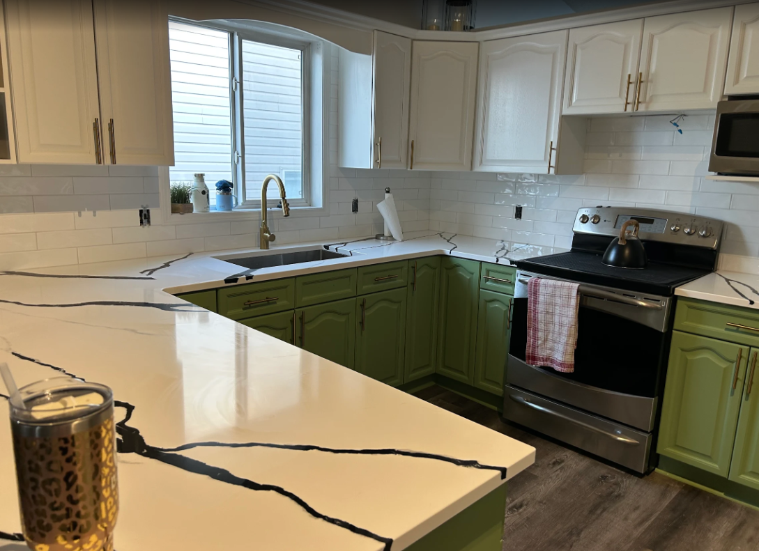 Bright kitchen with white countertops, white subway backsplash, green lower cabinets, and a window over the sink.