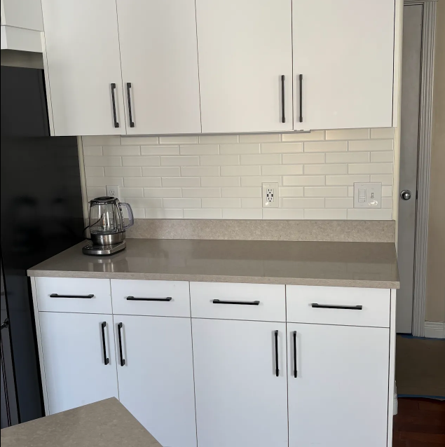 White kitchen cabinets and countertops with a kettle, backsplash, and tiled wall.