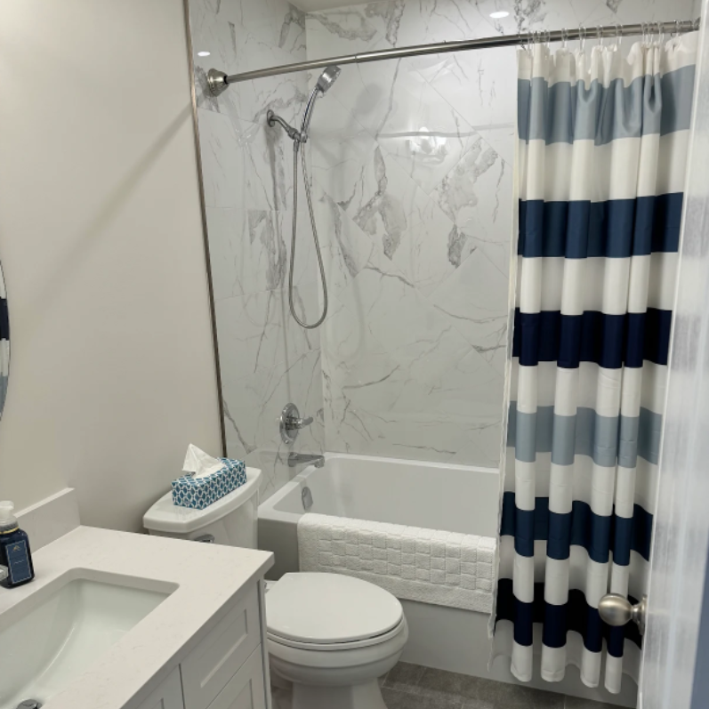 Small bathroom with shower, toilet, marble wall, and blue-and-white striped curtain
