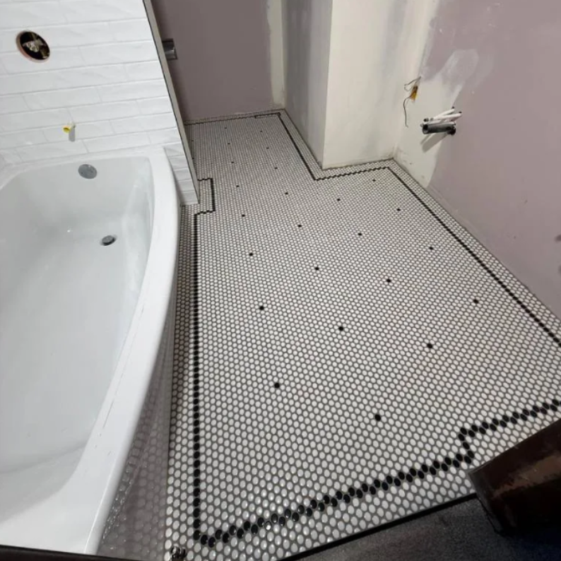 Small bathroom with a white bathtub and white hex tile floor, showing an unfinished wall and exposed plumbing.