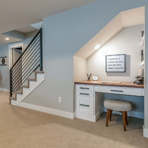 Built-in home office nook with desk, stool, and staircase beside a carpeted hallway