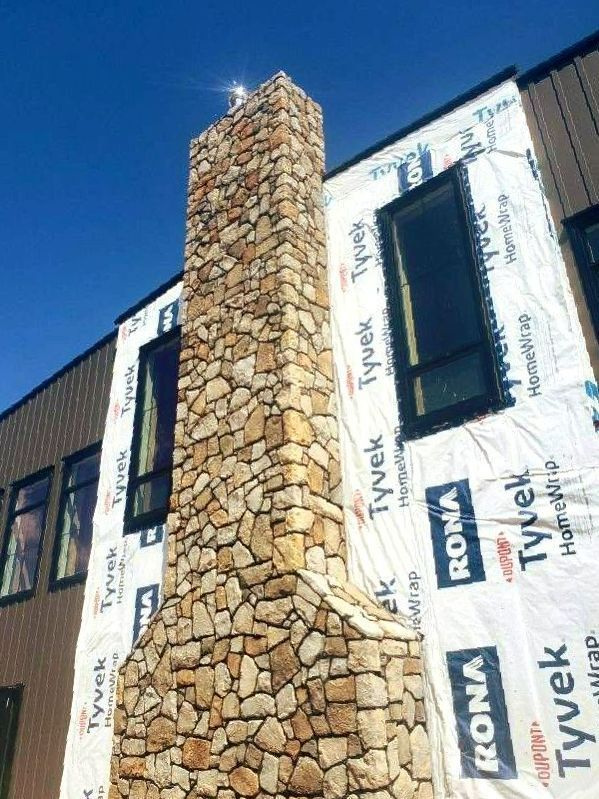 Stone chimney on house under construction, against a clear blue sky.