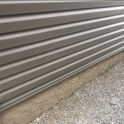 Gray siding on a building with a gravel base.