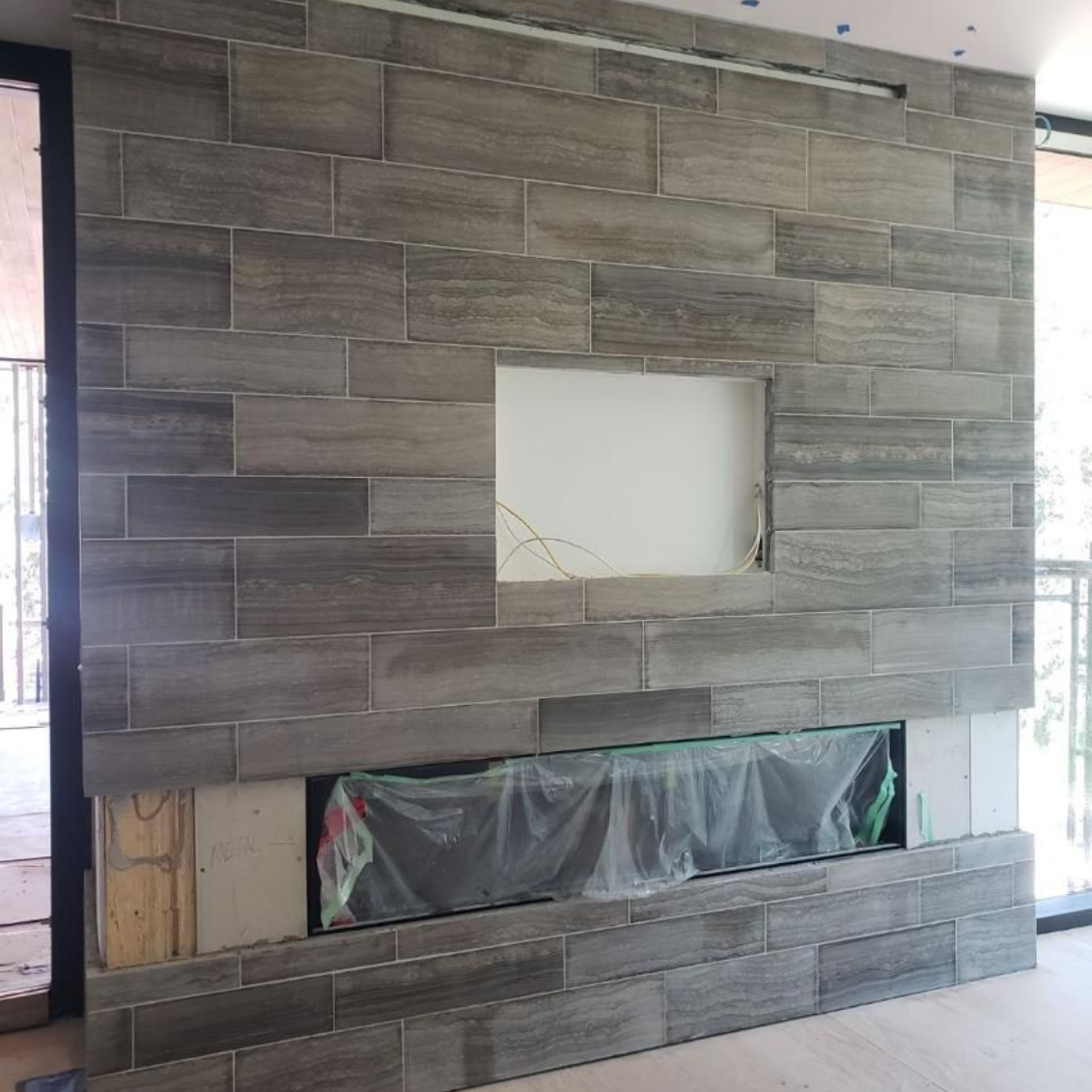 Gray stone fireplace with a rectangular opening and lower opening covered in plastic sheeting