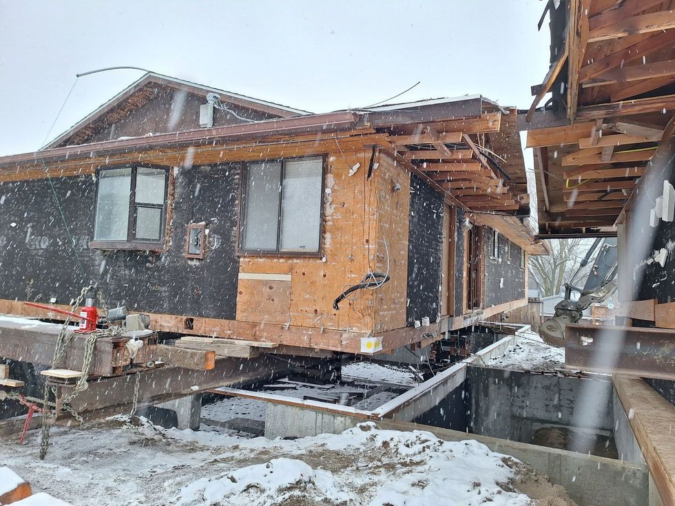A house being lifted off its foundation by steel beams during a snowy construction project.