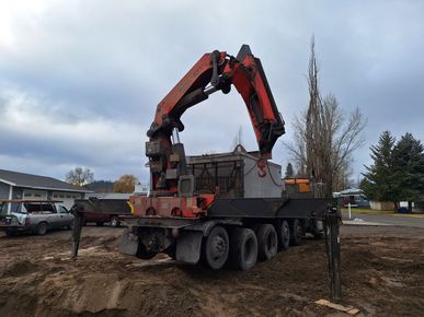 A red crane truck on a muddy job site lowering a large concrete structure into an excavation.
