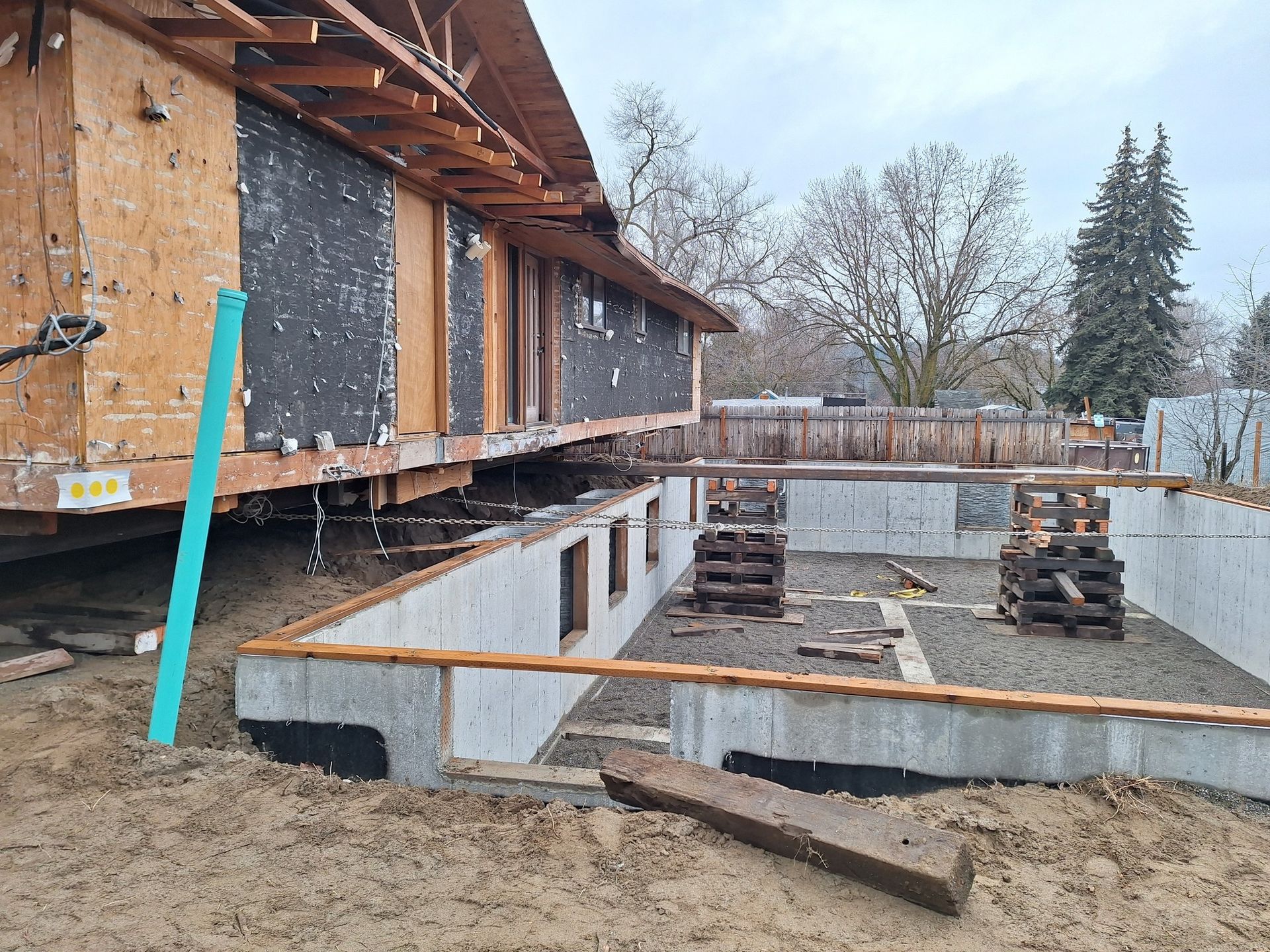 A residential building structure raised on steel beams above a new concrete foundation under construction.